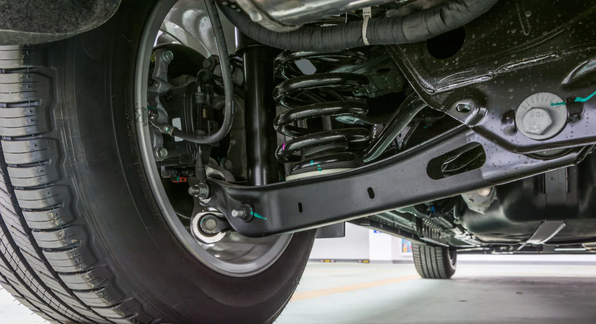 Underside of a vehicle showing front suspension components including coil spring, strut and control arm
